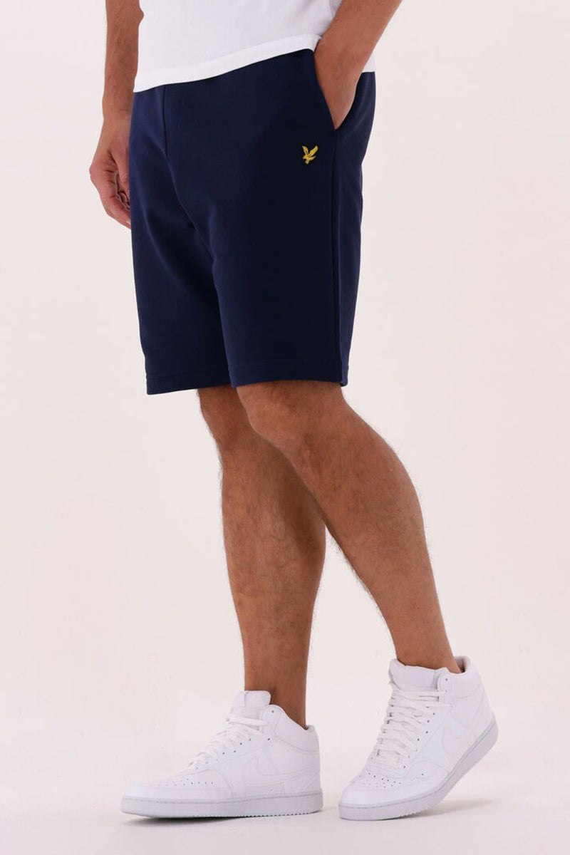 Korte blauwe short van LYLE & SCOTT, met een lengte tot halverwege het dijbeen, gedragen met witte hoge schoenen en een wit T-shirt.
