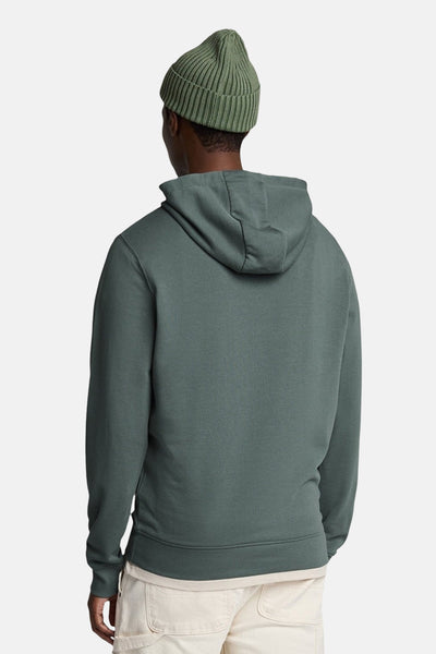 Sweat à capuche kaki de LYLE & SCOTT, avec une capuche, porté avec un bonnet et un pantalon beige.