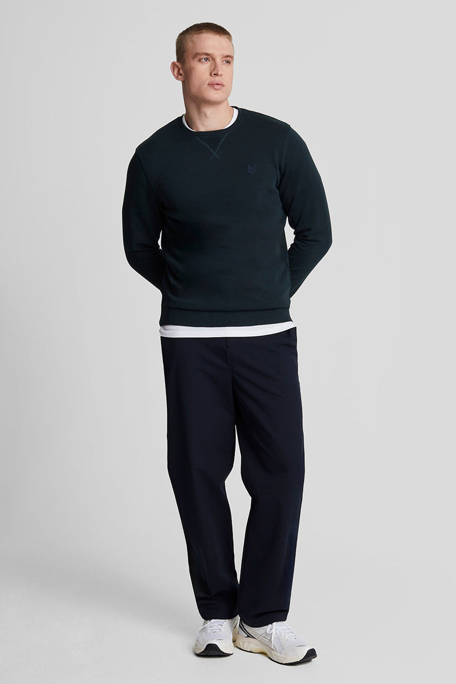 Blauwe sweater van LYLE & SCOTT met een ronde hals, gedragen over een wit T-shirt en een marineblauwe broek.