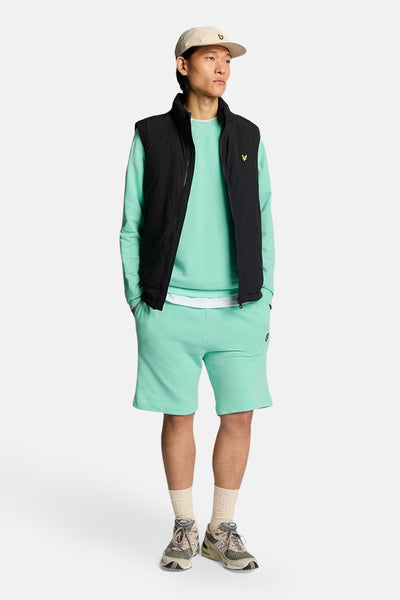 Sweat-shirt turquoise par LYLE & SCOTT, porté avec un gilet noir et un short assorti.