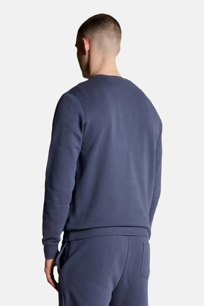 Sweat bleu de LYLE & SCOTT, vue de dos, porté avec un pantalon de survêtement assorti.