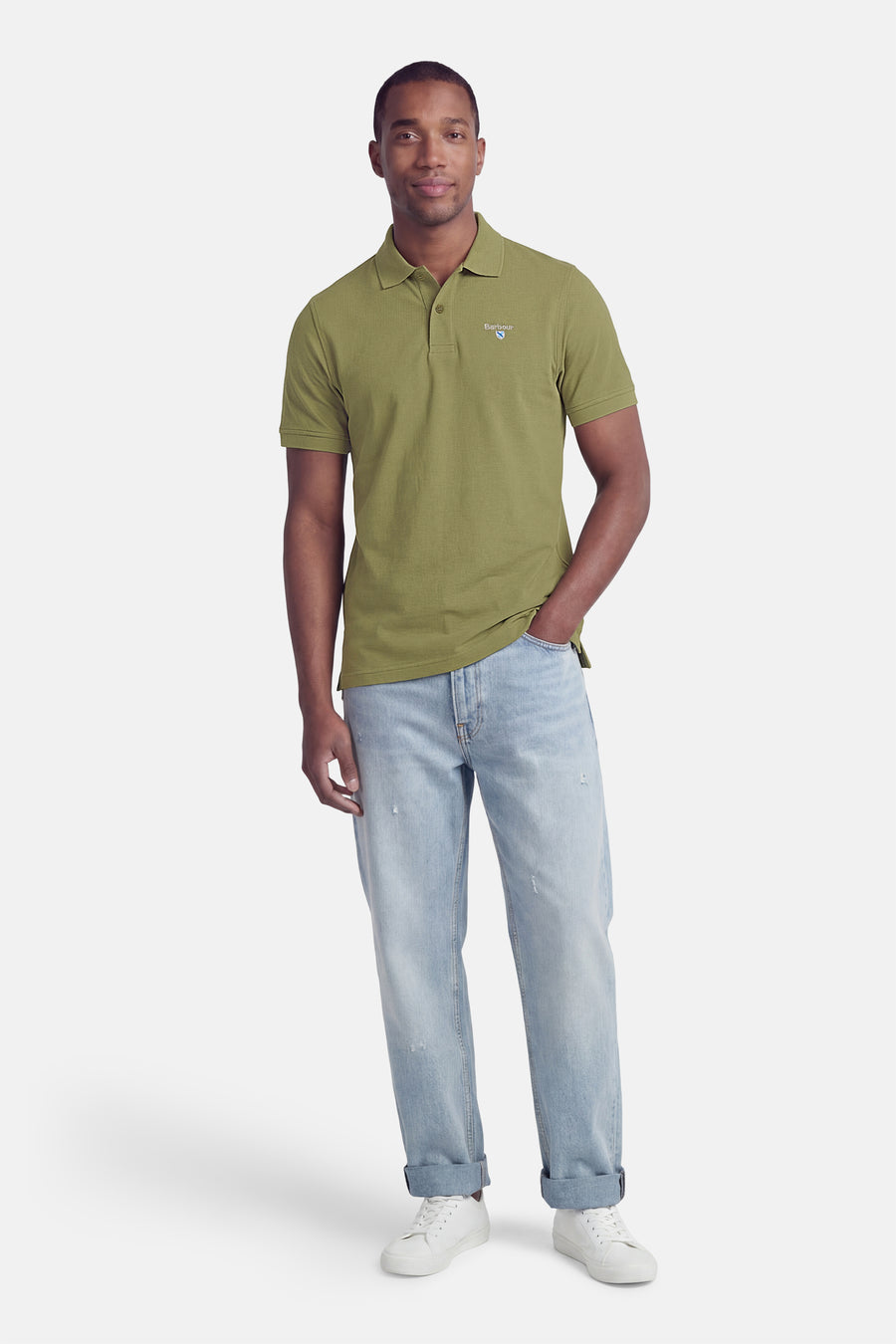 Polo vert à manches courtes de Barbour Classic, avec logo sur la poitrine et texture piquée, porté avec un jean clair et des baskets blanches.