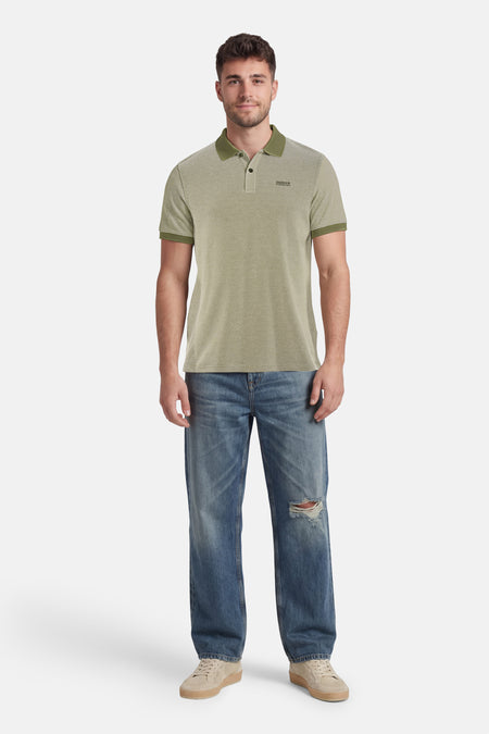 Groen poloshirt met microdessin van BARBOUR, gedragen door een man in gescheurde jeans en beige sneakers.