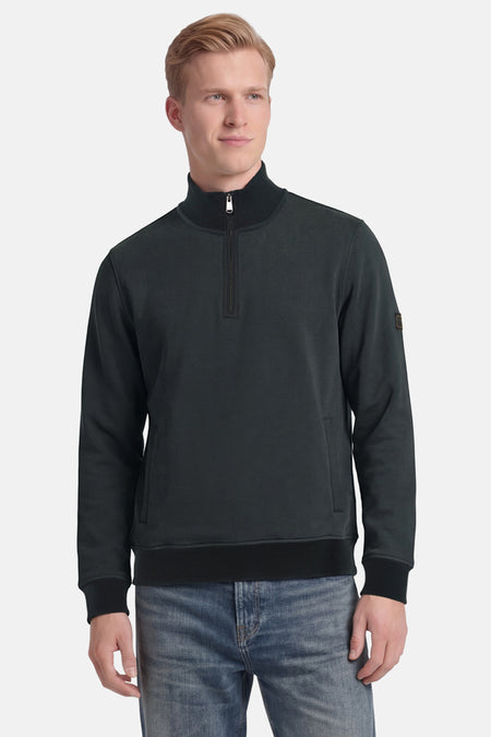 Groene trui met opstaande kraag van BARBOUR met korte ritssluiting, geribde kraag en patch op de mouw, gedragen met een spijkerbroek.