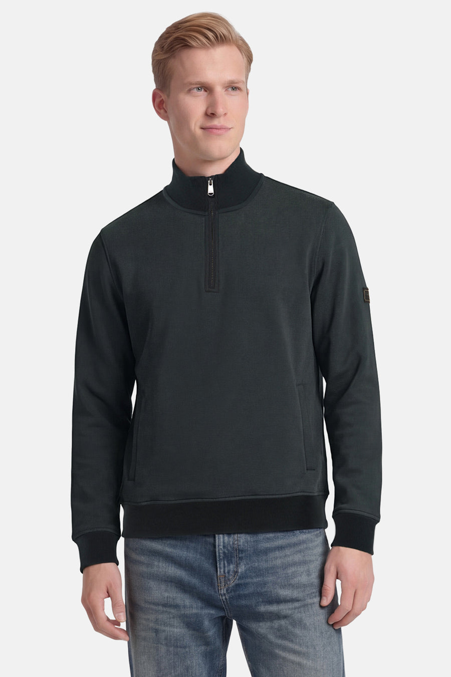 Sweat col montant vert de BARBOUR avec fermeture éclair courte, col côtelé et patch sur la manche, porté avec un jean.