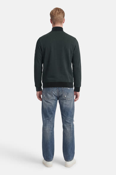 Sweat col montant vert foncé de BARBOUR avec poignets et ourlet côtelés, porté de dos avec un jean déchiré et des baskets blanches.