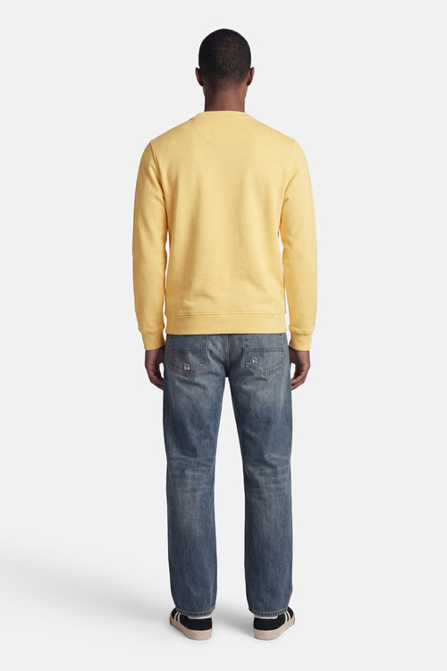 Gele rondehals sweatshirt van BARBOUR met subtiele textuur, achtergezicht op een model met een verbleekte spijkerbroek en sneakers.