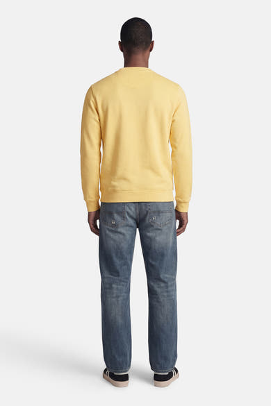 Gele rondehals sweatshirt van BARBOUR met subtiele textuur, achtergezicht op een model met een verbleekte spijkerbroek en sneakers.