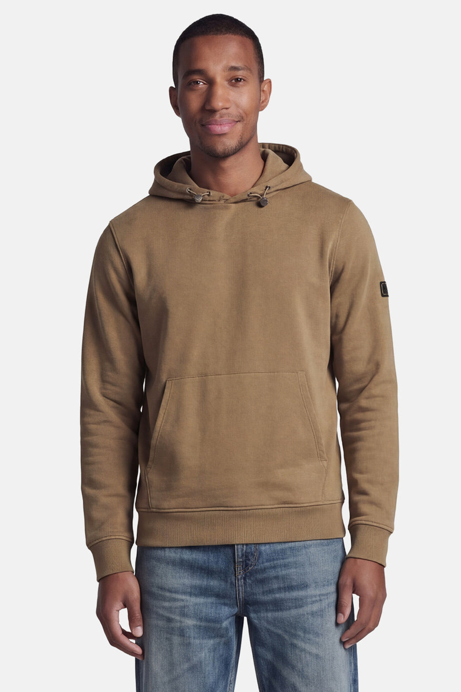 Beige hoodie van BARBOUR met kangoeroezak en zwart embleem op de mouw, gedragen door een man in een blauwe jeans.
