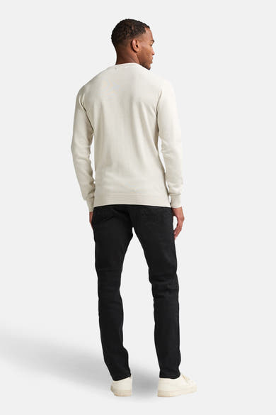 Pull à col rond écru de Petrol Industries, porté avec un pantalon noir et des baskets blanches, vue de dos.
