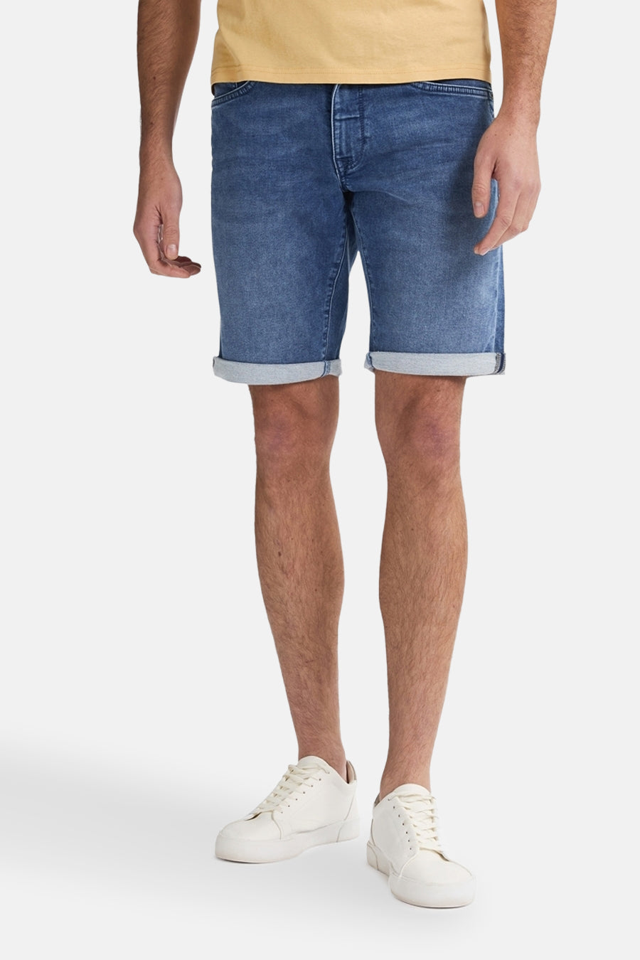 Korte donkerblauwe spijkerbroek van Petrol Industries, met omgeslagen zomen en gedragen met witte sneakers.