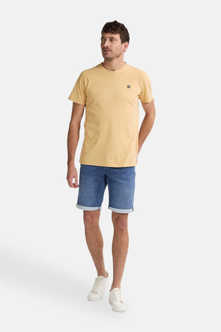 Korte donkerblauwe spijkerbroek van Petrol Industries, gedragen met een geel T-shirt en witte sneakers.