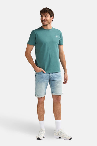 Lichtblauwe spijkerbroek van Petrol Industries, gedragen met een groen T-shirt en witte sneakers.