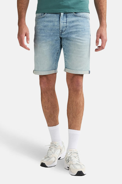 Lichtblauwe spijkerbroek van Petrol Industries, met opgerolde zomen, gedragen met witte sokken en lichte sneakers.