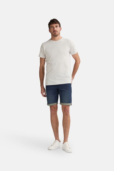Korte spijkerbroek in donkerblauw van Petrol Industries, gedragen met een lichtgrijs T-shirt en witte sneakers.