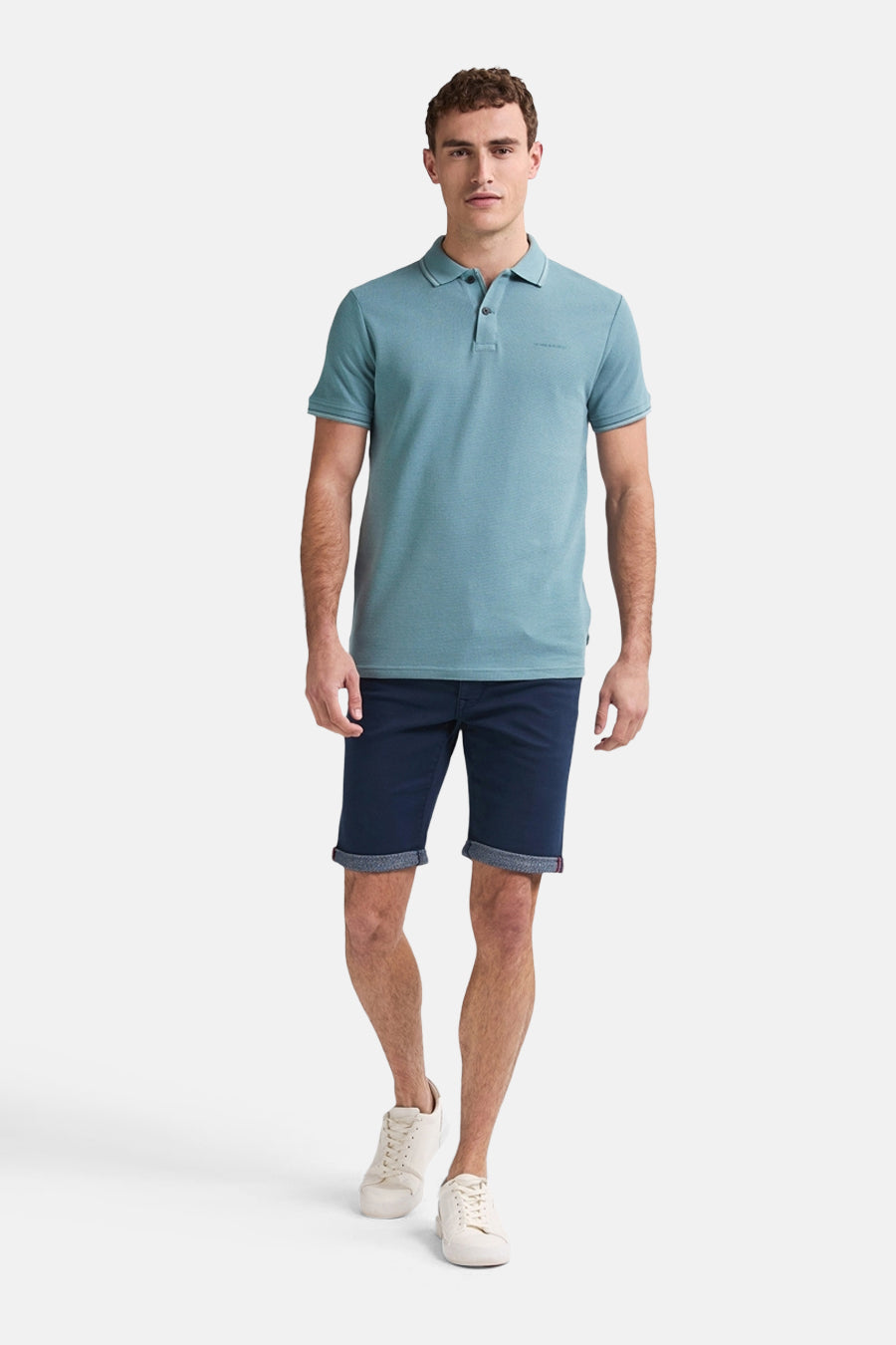 Short bleu foncé de Petrol Industries, avec revers et porté avec un polo bleu et des baskets blanches.
