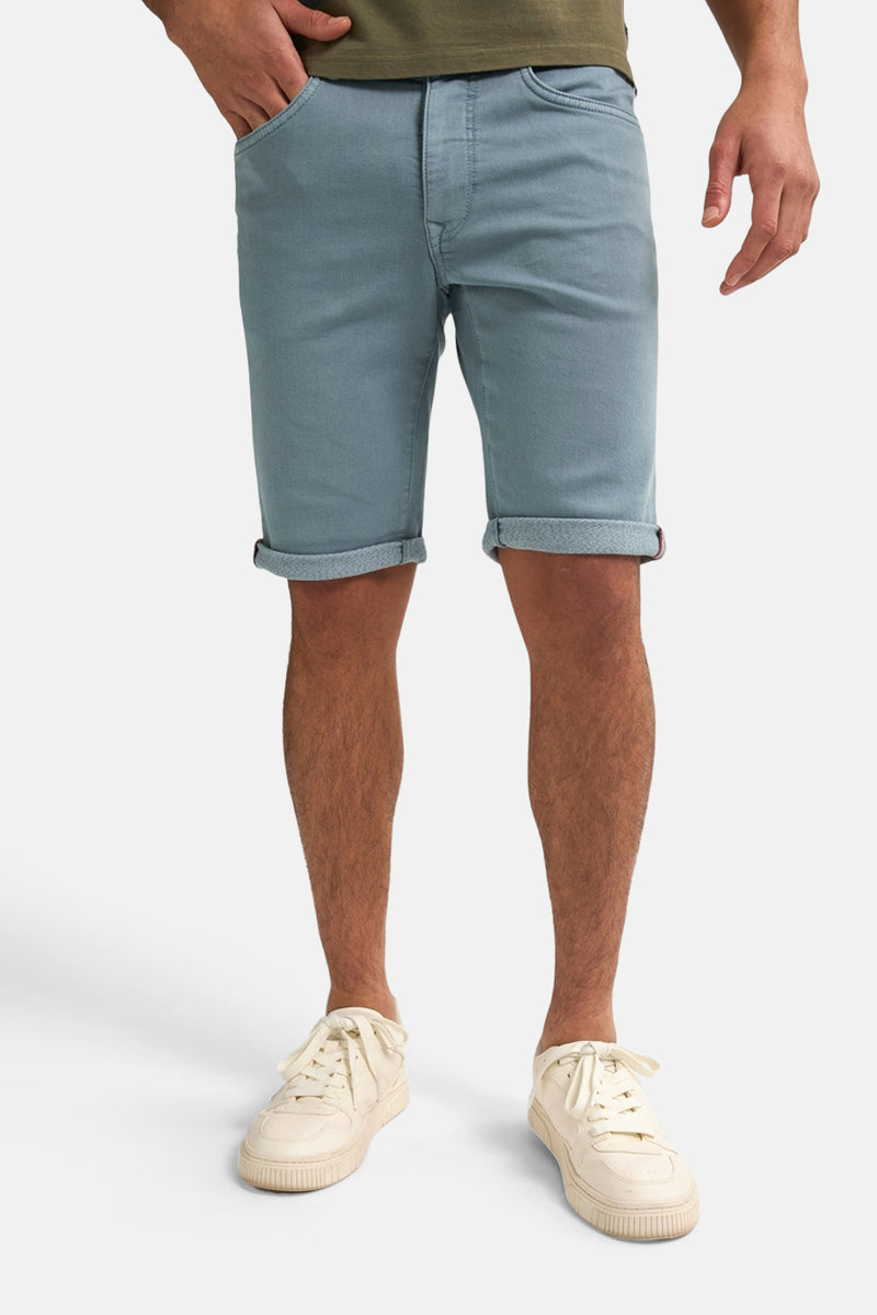 Korte blauwe spijkerjas van Petrol Industries, gedragen met crèmekleurige sportschoenen en een olijfgroen T-shirt.