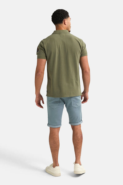 Korte blauwe spijkerbroek van Petrol Industries, gedragen met een olijfgroen poloshirt en witte sneakers.