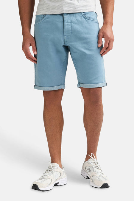 Korte blauwe short van Petrol Industries® met omgeslagen zomen, gedragen met een gestreept T-shirt en witte sneakers.