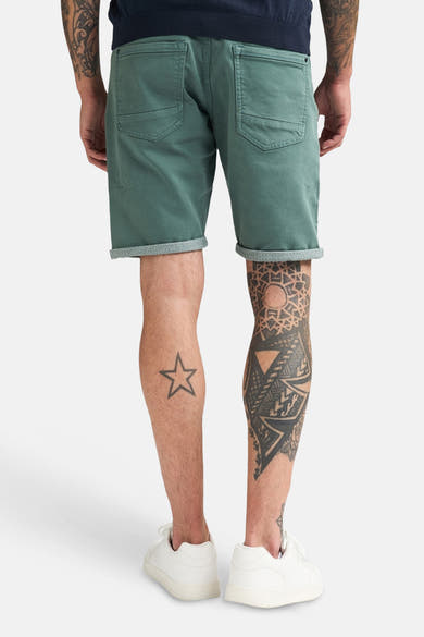 Korte groene short van Petrol Industries, rug van een man die de short draagt met omslag, achterzakken en witte sneakers.
