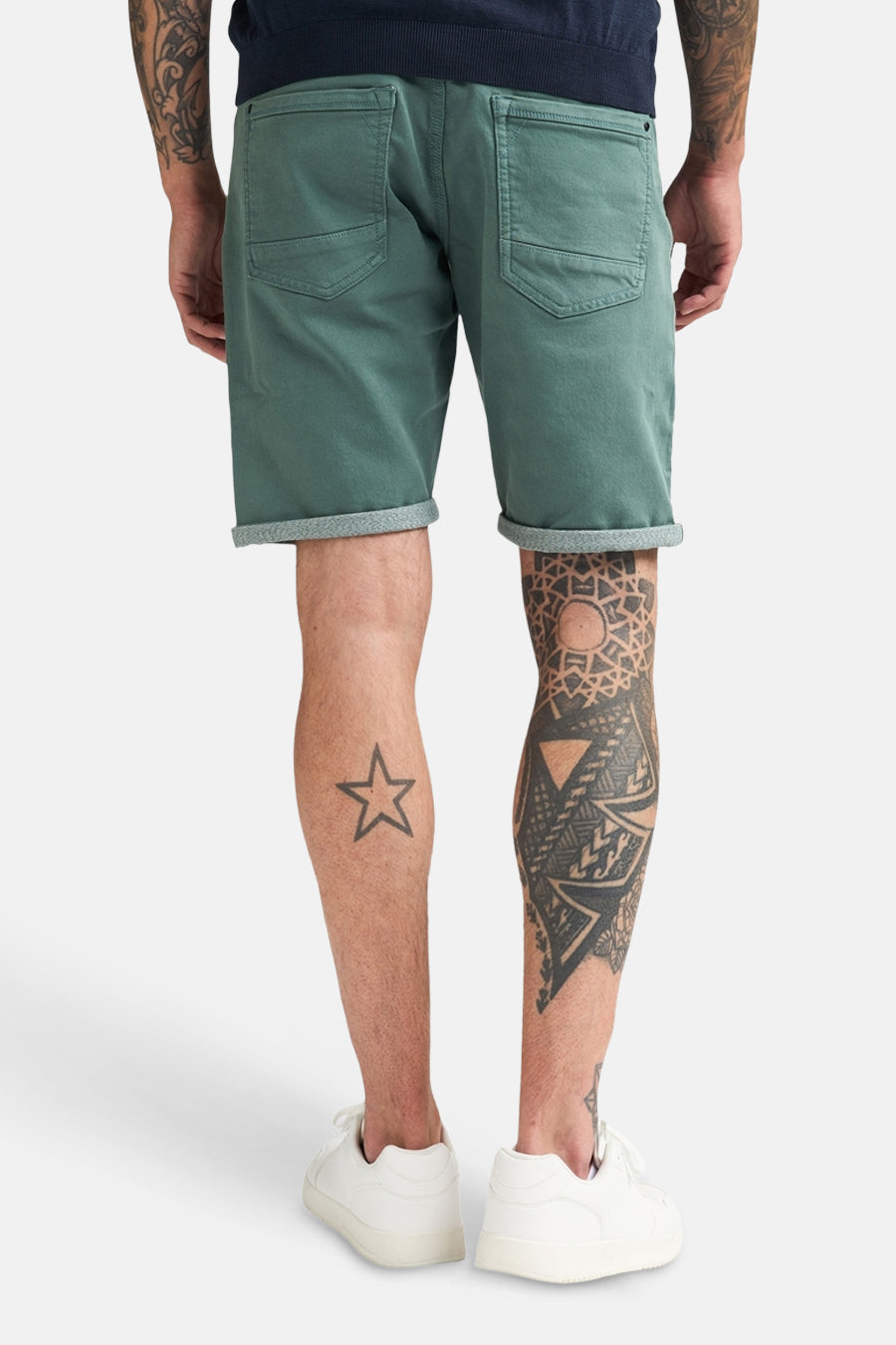 Korte groene short van Petrol Industries, rug van een man die de short draagt met omslag, achterzakken en witte sneakers.
