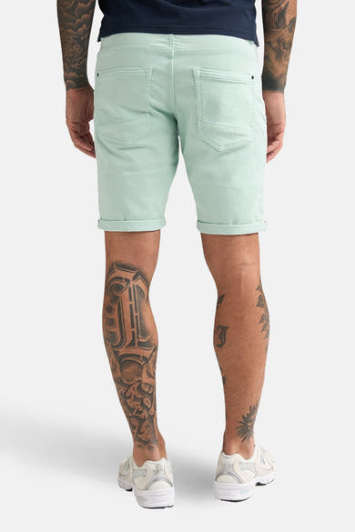Kort groen Petrol Industries® jack, model met revers, gedragen met een marineblauw T-shirt en witte schoenen.