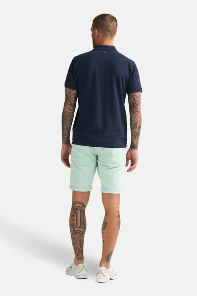 Kort groen Petrol Industries T-shirt, met opgerolde zoom en gedragen met een marineblauw poloshirt.