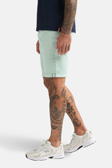 Korte groene Petrol Industries, gedragen met een marineblauw T-shirt en witte sneakers, in close-up.