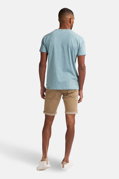 Short beige de Petrol Industries, avec ourlets retournés, porté avec un t-shirt bleu et des chaussures blanches.