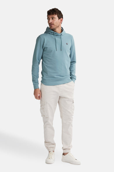 Sweat à capuche bleu de Petrol Industries, avec cordon de serrage, porté avec un pantalon cargo beige et des baskets blanches.
