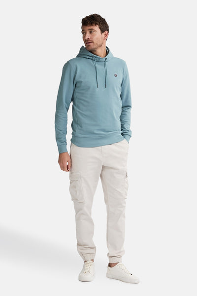 Sweat à capuche bleu de Petrol Industries, avec cordon de serrage, porté avec un pantalon cargo beige et des baskets blanches.
