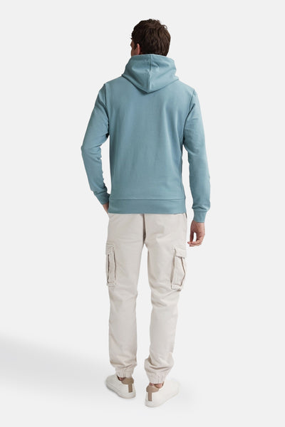 Sweat à capuche bleu de Petrol Industries, vue de dos, porté avec un pantalon cargo et des chaussures de sport.