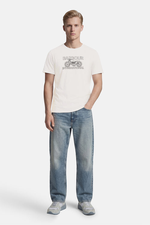 T-shirt blanc de BARBOUR à motif de moto et texte "BARBOUR INTERNATIONAL", porté avec un jean bleu et des baskets grises.