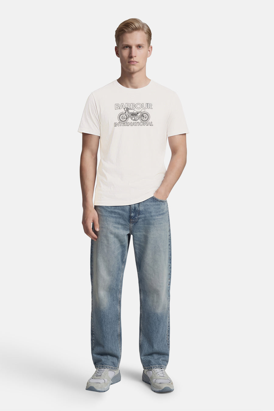 T-shirt blanc de BARBOUR à motif de moto et texte "BARBOUR INTERNATIONAL", porté avec un jean bleu et des baskets grises.