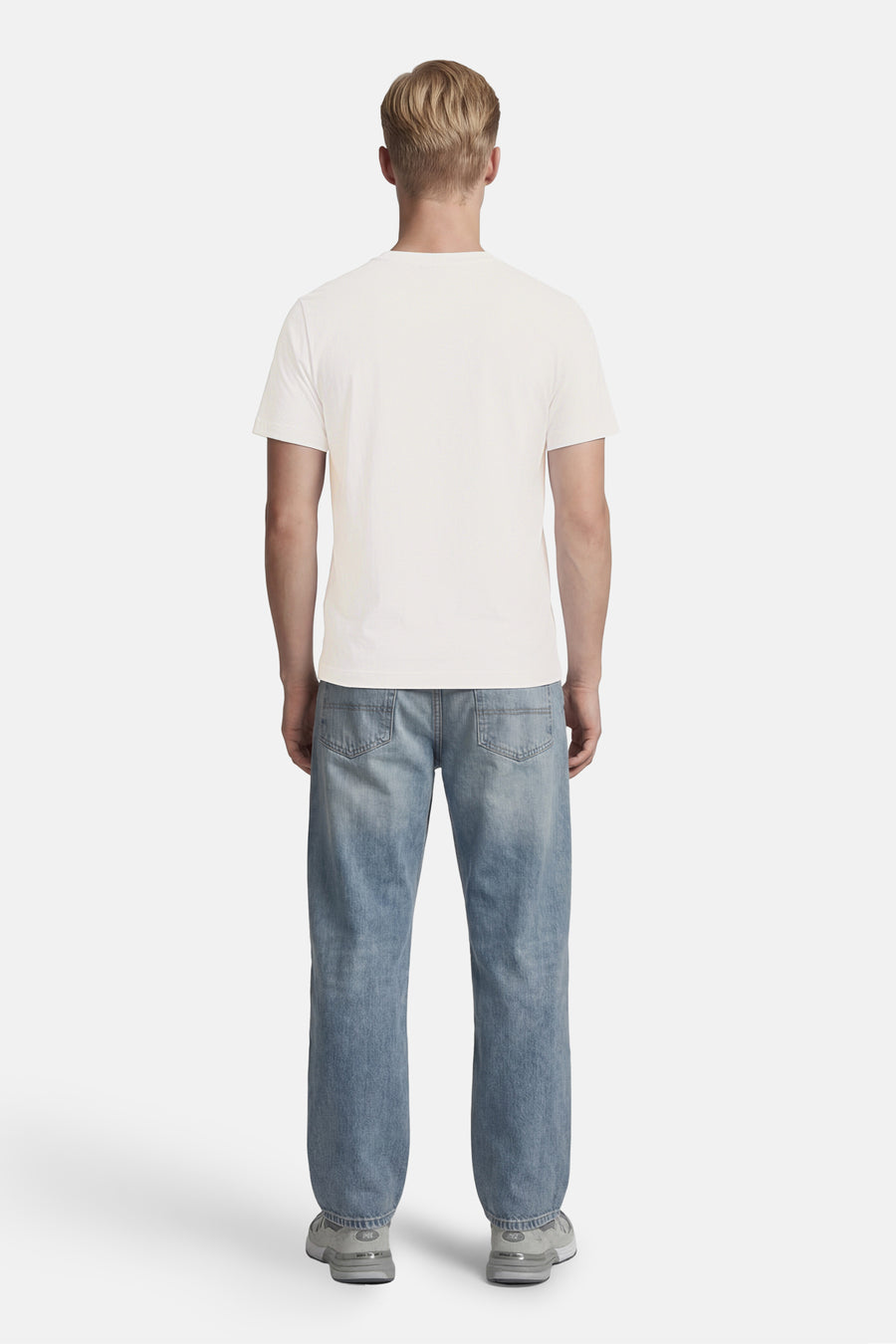 T-shirt blanc à manches courtes de BARBOUR, porté de dos par un homme avec un jean bleu clair et des baskets grises.