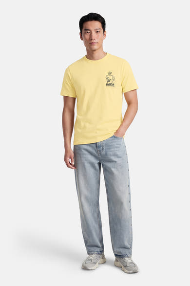T-shirt jaune à manches courtes de BARBOUR, avec un imprimé graphique sur le devant et porté avec un jean bleu délavé.
