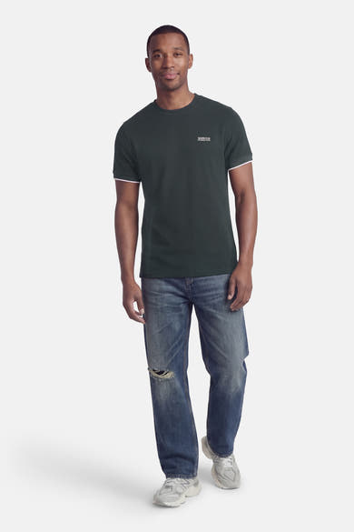 T-shirt à manches courtes vert, de Barbour, avec bordure contrastée aux manches et porté avec un jean décontracté.