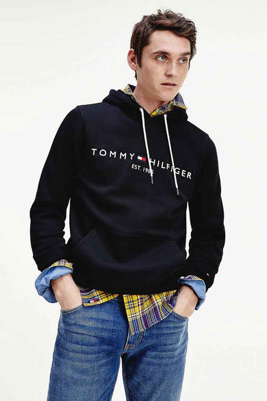 Sweat à capuche noir de TOMMY JEANS, avec cordon de serrage et poche kangourou, porté sur une chemise à carreaux.