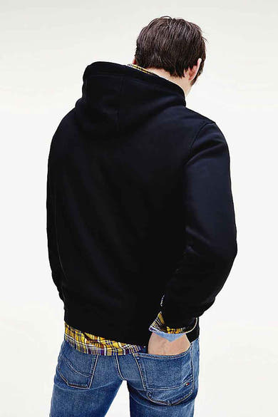 Sweat noir à capuche de TOMMY JEANS, porté sur une chemise à carreaux, avec un jean bleu.