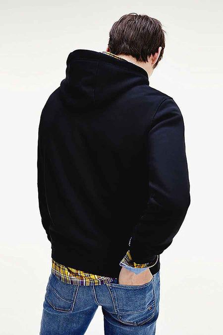 Sweat noir à capuche de TOMMY JEANS, porté sur une chemise à carreaux, avec un jean bleu.