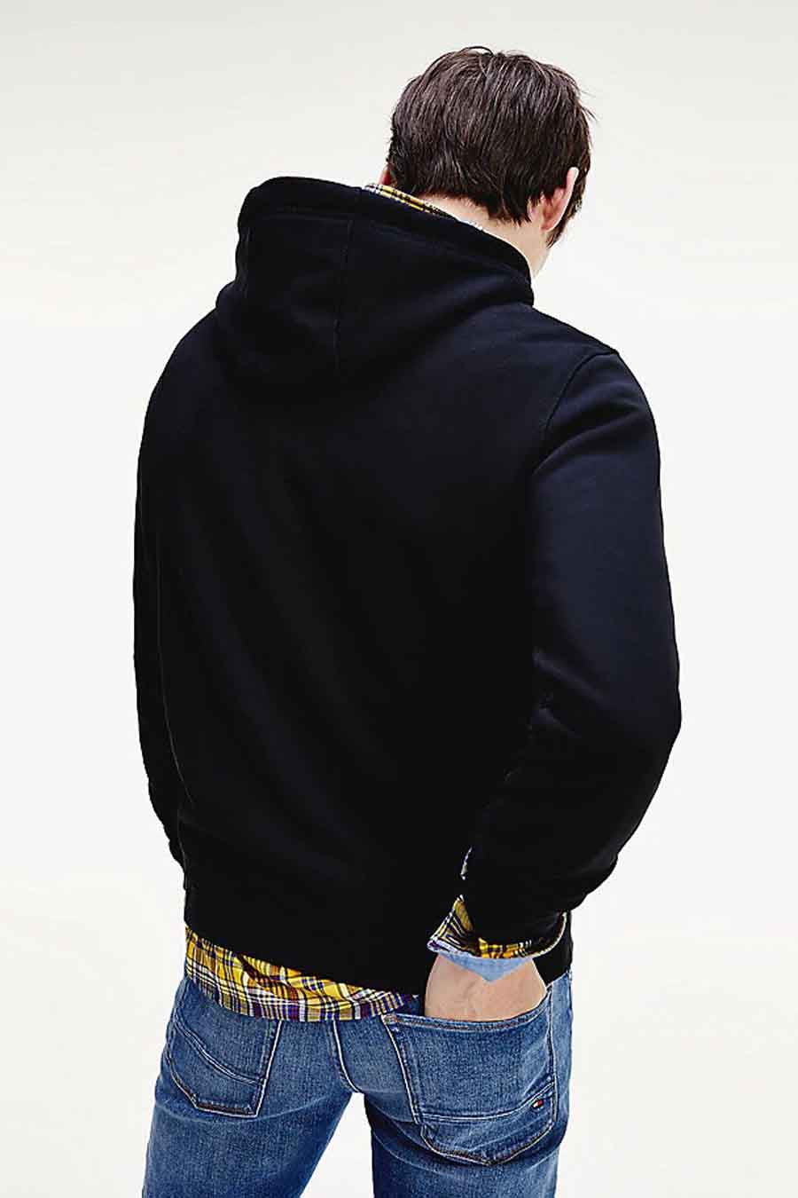 Sweat noir à capuche de TOMMY JEANS, porté sur une chemise à carreaux, avec un jean bleu.