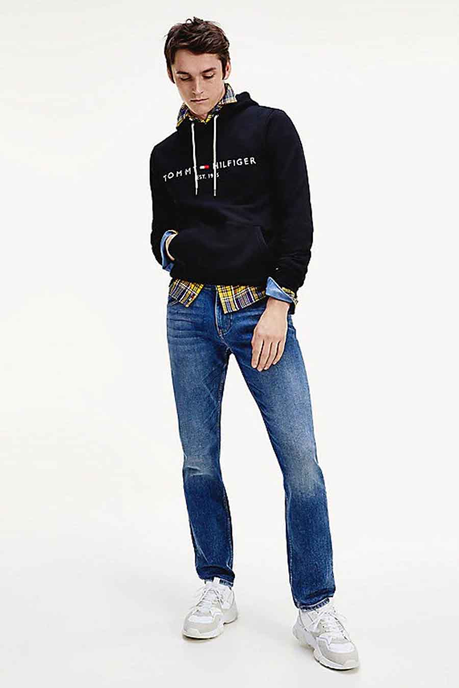 Sweat noir à capuche by TOMMY JEANS, porté sur une chemise à carreaux et un jean, avec des baskets blanches.