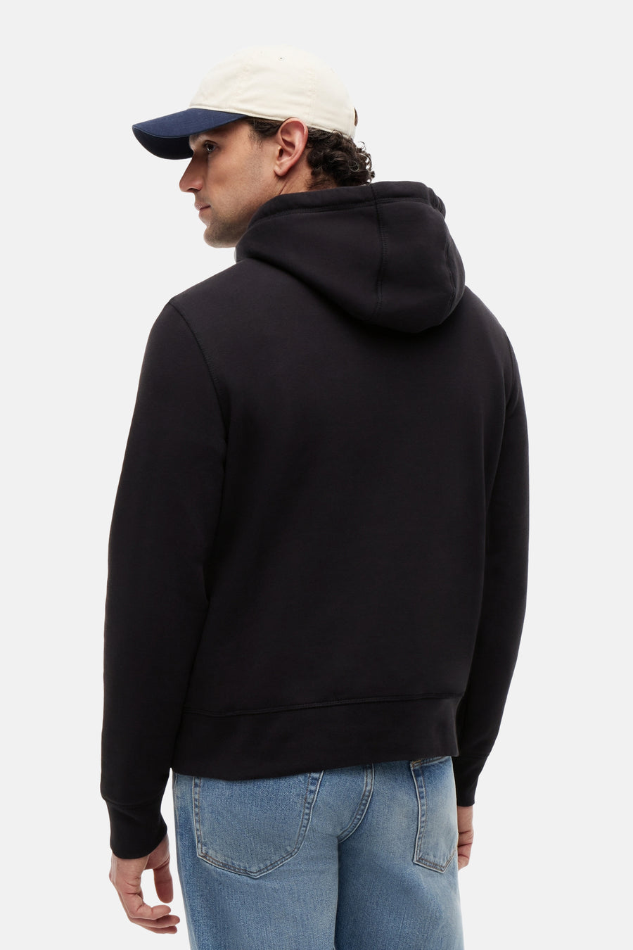 Sweat à capuche noir de TOMMY JEANS, vu de dos, avec une casquette bicolore et un jean bleu clair.