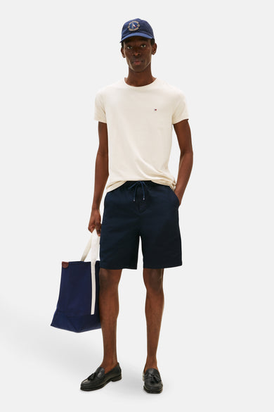 Beige T-shirt met korte mouwen van TOMMY HILFIGER, gedragen met een marineblauwe korte broek en zwarte loafers.