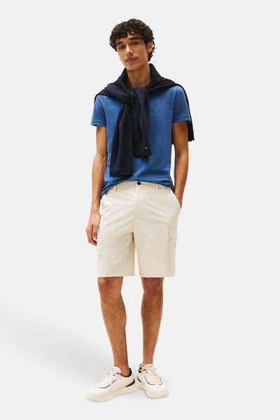 T-shirt bleu à manches courtes de TOMMY HILFIGER, porté avec un pull noué et un short cargo beige.