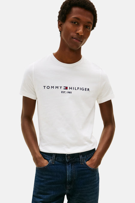 White short-sleeve T-shirt by TOMMY JEANS with navy and red logo print, worn with dark blue jeans, front view.