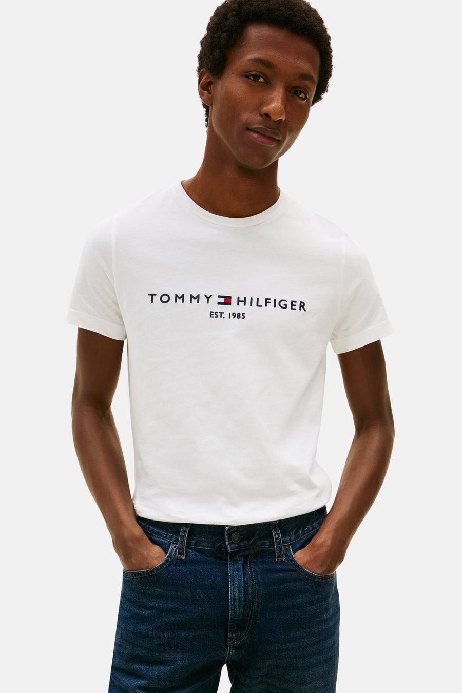 White short-sleeve T-shirt by TOMMY JEANS with navy and red logo print, worn with dark blue jeans, front view.