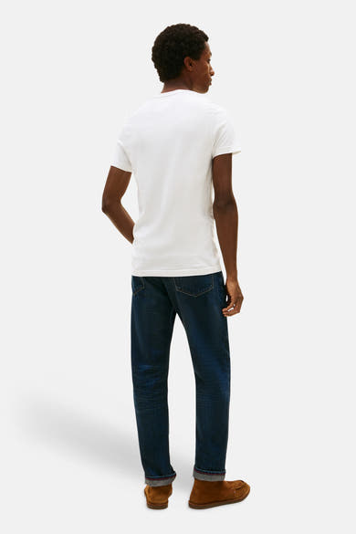White short-sleeve t-shirt by TOMMY JEANS, back view on model wearing dark denim jeans and brown suede shoes