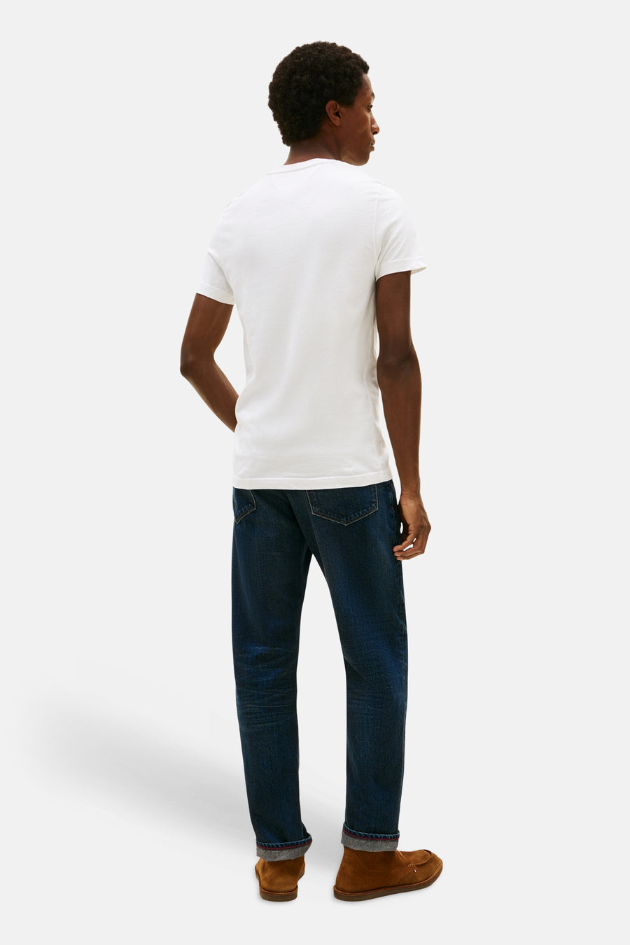 White short-sleeve t-shirt by TOMMY JEANS, back view on model wearing dark denim jeans and brown suede shoes