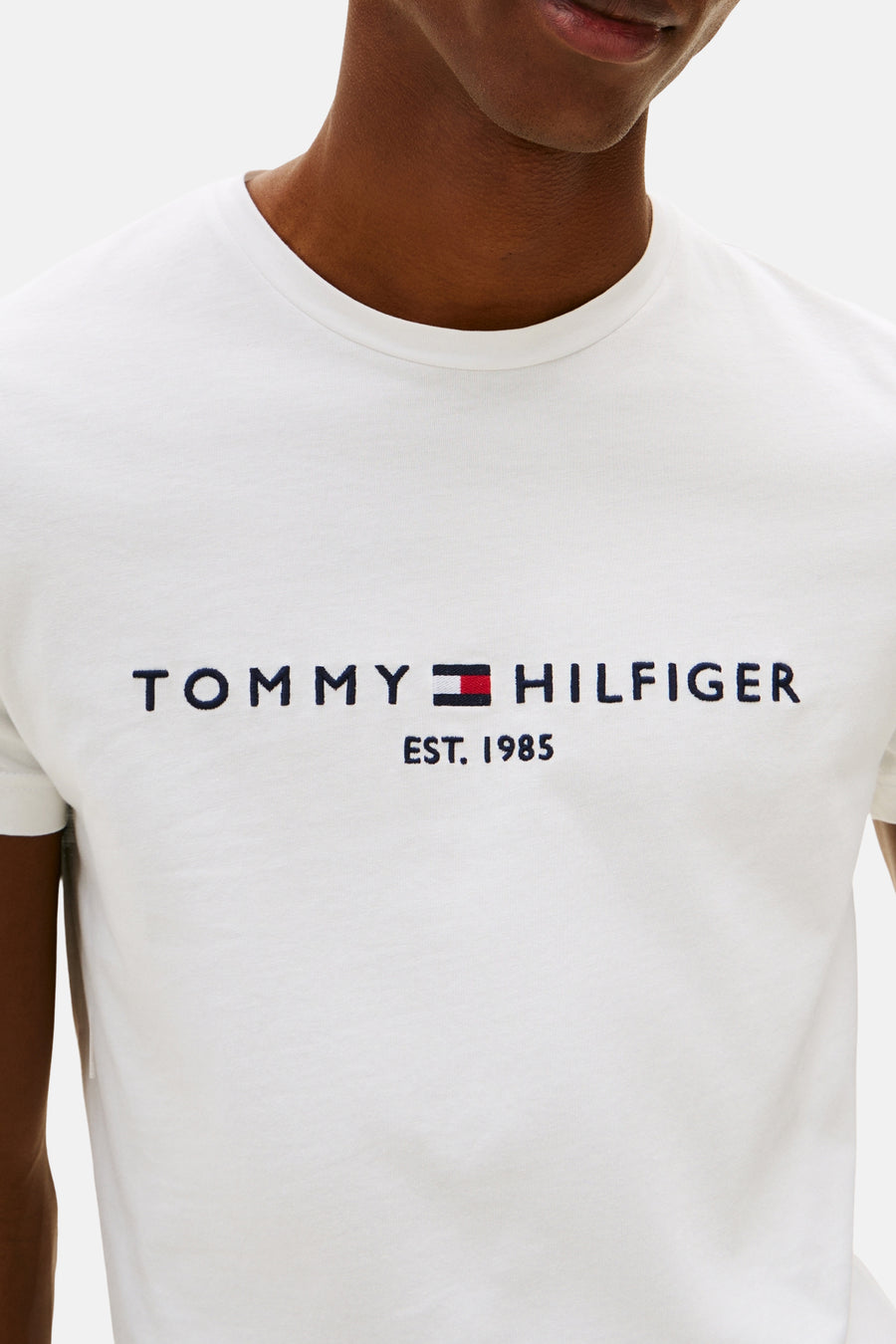 White short-sleeve T-shirt by TOMMY JEANS with embroidered Tommy Hilfiger logo and EST. 1985 text, front view on model